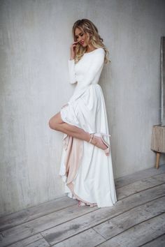 a woman in a white dress leaning against a wall with her leg on the floor