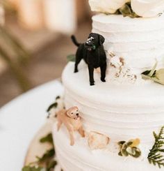 a wedding cake decorated with white flowers and black dog figurines