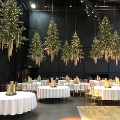 tables and chairs are set up with white tablecloths, gold candlesticks and christmas trees hanging from the ceiling