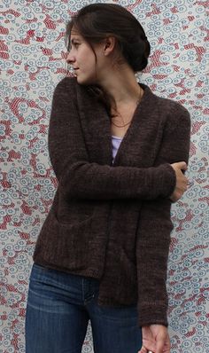 a woman standing in front of a wall with her hand on her hip and looking to the side