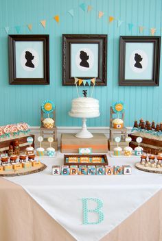 a table topped with cakes and cupcakes next to framed pictures on the wall