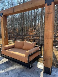 a brown couch sitting on top of a wooden porch swing bed next to a forest