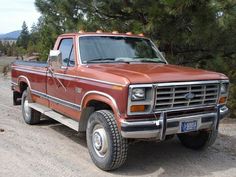 a red pick up truck parked on the side of a dirt road next to trees