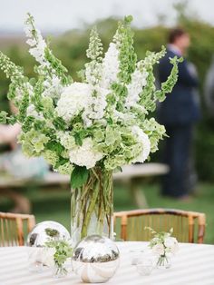 a vase filled with white flowers sitting on top of a table next to two silver balls