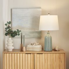 a wooden cabinet with two vases and a lamp on it next to a painting