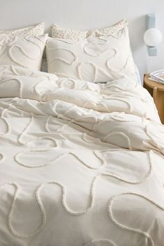 a bed with white comforter and pillows on top of it next to a night stand