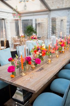 a long wooden table topped with lots of vases filled with colorful flowers and candles