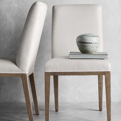 two white chairs sitting next to each other in front of a gray wall with a bowl on top