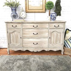 a white dresser with two vases on top of it and a clock mounted to the wall