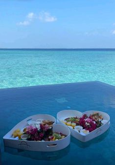 two white trays filled with food sitting on top of a swimming pool next to the ocean