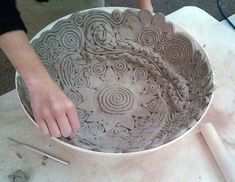 a person is working on a large bowl with intricate designs in the shape of spirals