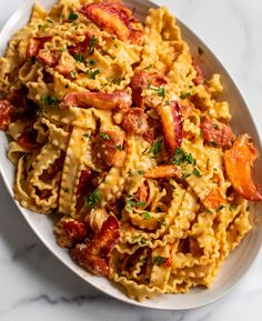 a white plate topped with pasta covered in bacon and tomato sauce on top of a marble table