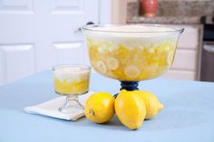 a glass bowl filled with lemons next to two glasses on a blue table cloth