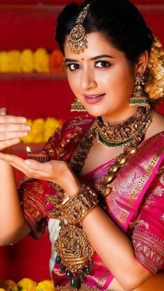 a woman in a red and gold sari with jewelry on her hands, posing for the camera