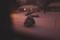 a snow covered street at night with cars parked in the driveway