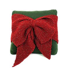 a red and green knitted pillow with a large bow on the top of it