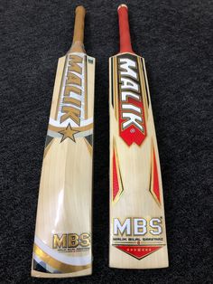 two cricket bats sitting on top of a black carpet