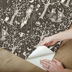 a person cutting paper on top of a table with an owl and skeleton wallpaper