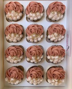 twelve cupcakes in a box with pink frosting and white flowers on them