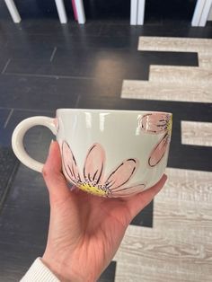 a hand holding a coffee cup with flowers painted on it