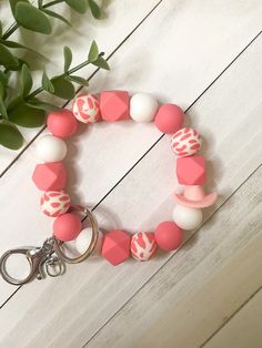 a pink and white beaded bracelet on a keychain next to a plant