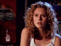 a woman with curly hair sitting in front of a book shelf