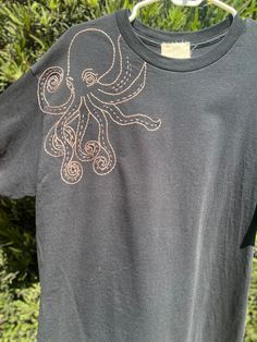 an octopus t - shirt is hanging on a clothes rack outside in front of some bushes