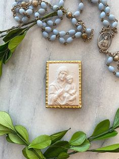 a necklace with a statue on it next to some green leaves and beads that are laying on the ground