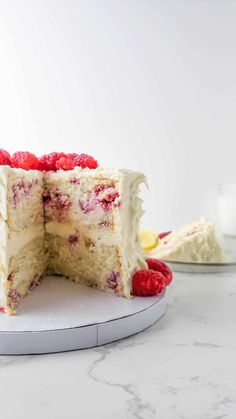 a cake with white frosting and raspberries cut in half