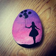 a painted rock with a silhouette of a girl holding balloons in the shape of a heart