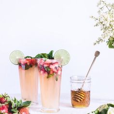 two glasses filled with liquid and strawberries next to flowers