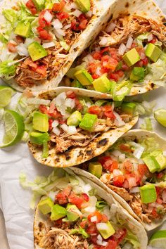 four tacos with shredded meat, avocado and tomatoes