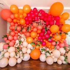 an arrangement of balloons and flowers on the floor in front of a wall made out of oranges, pinks, and white