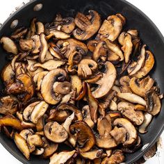 a skillet filled with mushrooms on top of a table next to utensils