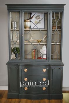 an old china cabinet with glass doors painted in dark gray and gold trimmings