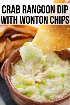 a hand dipping some potato chips into a bowl of crab rangoon dip with wonton chips