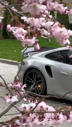 a white sports car is parked in front of some pink flowers