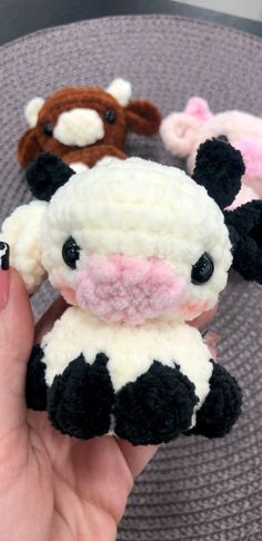 a hand holding a small stuffed cow in it's right hand and three other knitted animals behind it