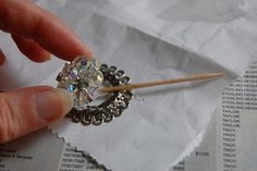 a person holding a small diamond on top of a piece of paper with a toothpick in it