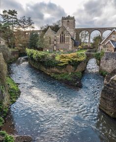 a river running through a lush green countryside next to a stone bridge and old buildings