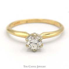 a yellow gold engagement ring with a round diamond in the center, on a white background