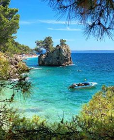 there is a boat that is in the water near some rocks and trees on the shore