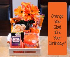 an orange gift box filled with treats and flowers on a table next to a sign that says, orange you glad it's your birthday?