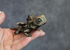 a small lizard sitting on top of someone's hand in front of a gray background