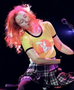 a woman with long red hair is playing the piano in front of a microphone on stage