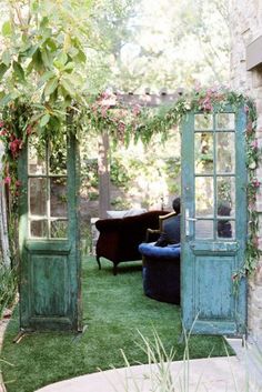 an old door is open on the grass in front of a couch and table with flowers