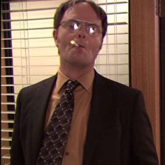 a man wearing glasses and a tie standing in front of a window with blinds on it