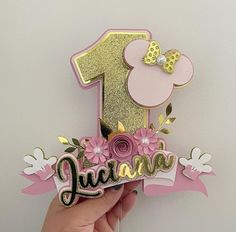 a hand holding up a pink and gold first birthday card with the number one on it