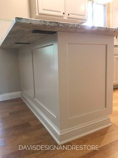 an island in the middle of a kitchen with white cupboards and wood flooring