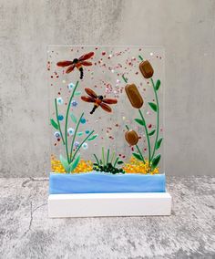 a glass block with dragonflies and flowers in it on a table next to a wall